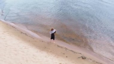 Elbiseli genç bir kadın sahil boyunca koşuyor. Hava çekimi