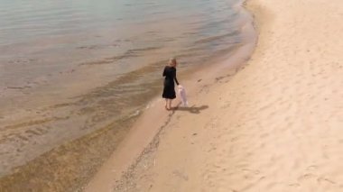 Elbiseli genç bir kadın sahil boyunca koşuyor. Hava çekimi