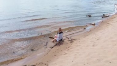 Elbiseli genç bir kadın sahil boyunca koşuyor. Hava çekimi