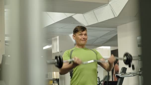 Een man met overgewicht liften een EZ barbell terwijl staan in de sportschool. Oefening voor biceps. Fitness. Gezonde levensstijl. — Stockvideo