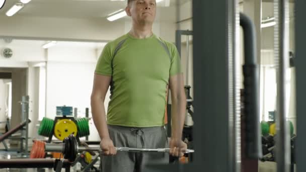 A overweight man lifts an ez barbell while standing at the gym. Exercise for biceps. Fitness. Healthy lifestyle. — Stock Video