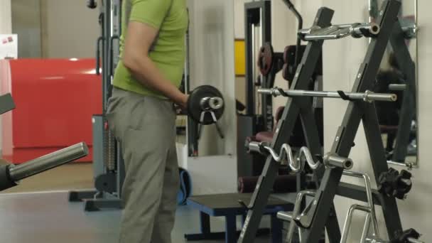 Un hombre con sobrepeso levanta una barra de ez mientras está parado en el gimnasio. Ejercicio para bíceps. Fitness. Estilo de vida saludable . — Vídeo de stock