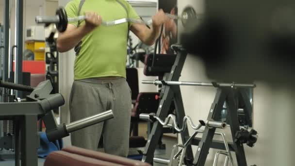 Un hombre con sobrepeso levanta una barra de ez mientras está parado en el gimnasio. Ejercicio para bíceps. Fitness. Estilo de vida saludable . — Vídeos de Stock