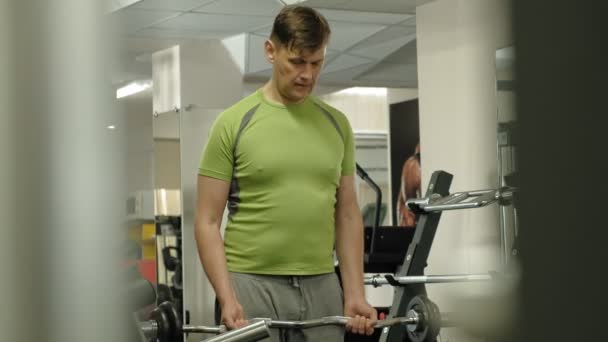 Un hombre con sobrepeso levanta una barra de ez mientras está parado en el gimnasio. Ejercicio para bíceps. Fitness. Estilo de vida saludable . — Vídeos de Stock