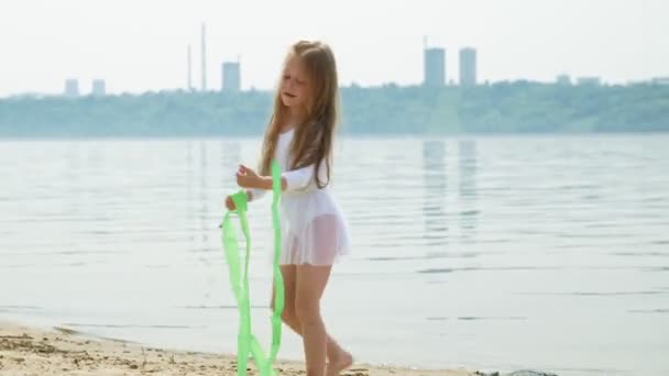 Νηπιαγωγείο κορίτσι με χορούς μια γυμναστική κορδέλα σε μια αμμώδη παραλία. Καλοκαίρι, αυγή — Αρχείο Βίντεο