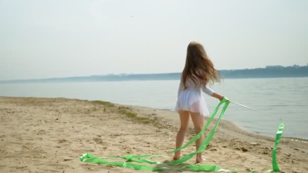 Předškolní dívka s tancuje gymnastickou stuhu na písečné pláži. Léto, svítání — Stock video