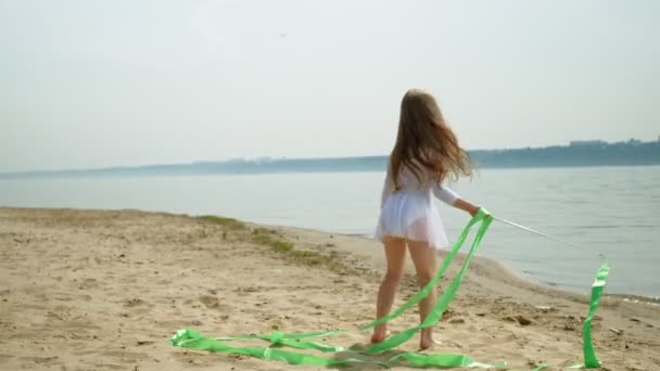 Preschool girl with dances a  gymnastic ribbon on a sandy beach. Summer, dawn — Stock Video