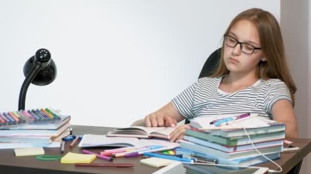 En tonåring flicka med glasögon sitter på en skola skriv bord. lärande koncept — Stockvideo