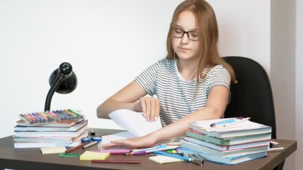Ένα έφηβο κορίτσι με γυαλιά κάθεται σε ένα σχολικό γραφείο. έννοια της μάθησης — Αρχείο Βίντεο