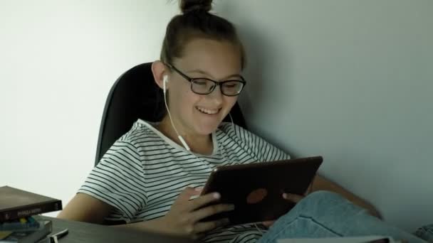 Chica adolescente utiliza la tableta con auriculares. Hora de la tarde. — Vídeos de Stock