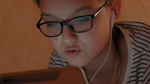 Tini lány használja tabletta fejhallgatóval. Esti idő — Stock videók