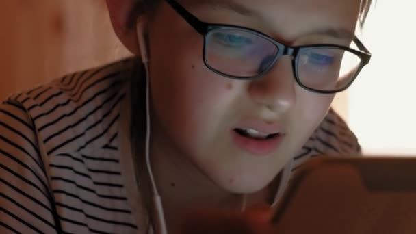 Дівчина-підліток використовує планшет з навушниками. Вечірній час — стокове відео