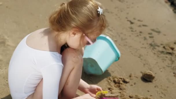 Meisje kind speelt met zand op het strand met behulp van mallen beeldjes. Zonnige zomerdag. Vakantie — Stockvideo