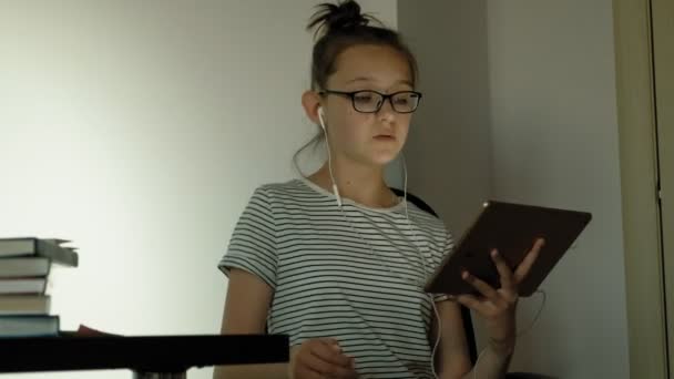 Девочка-подросток пользуется планшетом с наушниками. Вечернее время — стоковое видео