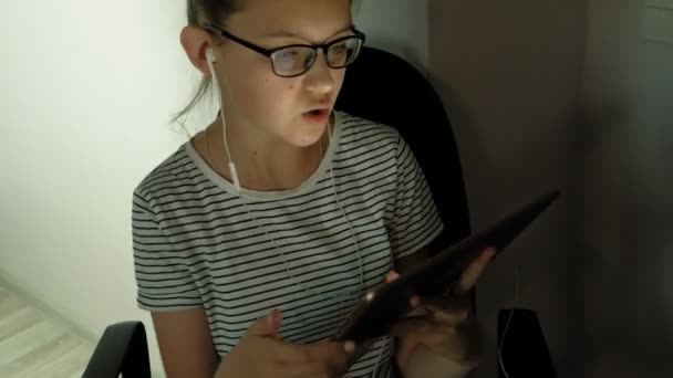 Teen girl utilise une tablette avec écouteurs. Heure du soir — Video