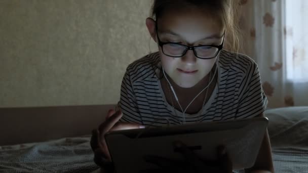 Chica adolescente utiliza la tableta con auriculares. Hora de la tarde. — Vídeo de stock