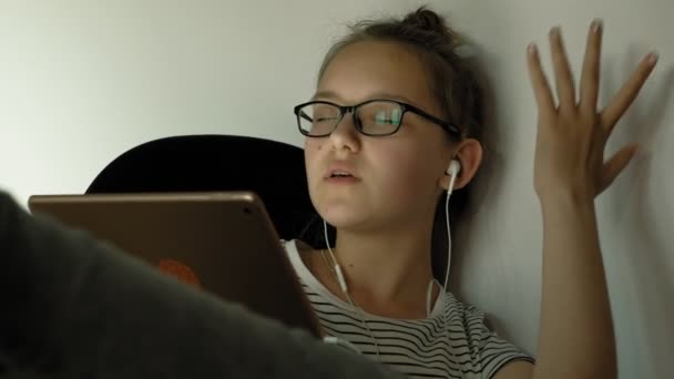 Tiener meisje maakt gebruik van tablet met hoofdtelefoon. Avond tijd — Stockvideo