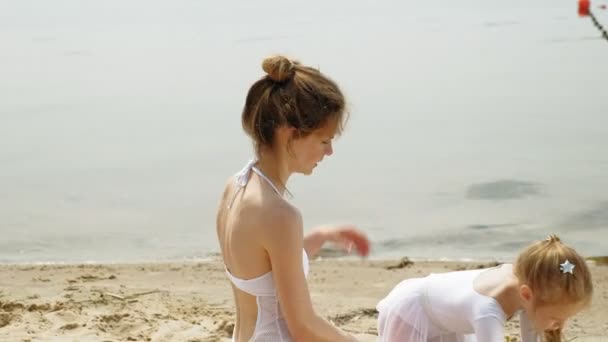 Mère et fille en maillots de bain blancs dansant avec un ruban de gymnastique sur une plage de sable fin. Été, aube — Video