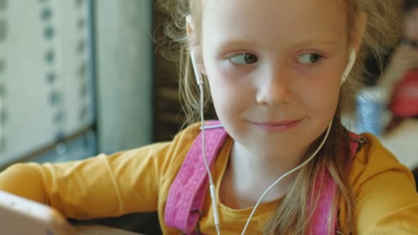 Preschool girl uses headphones computer tablet indoors — Stock Video