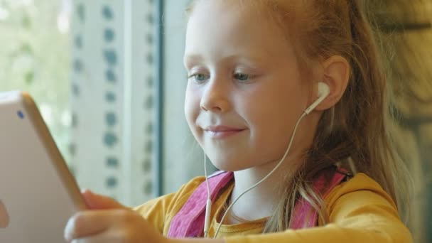 Preschool girl uses headphones computer tablet indoors — Stock Video