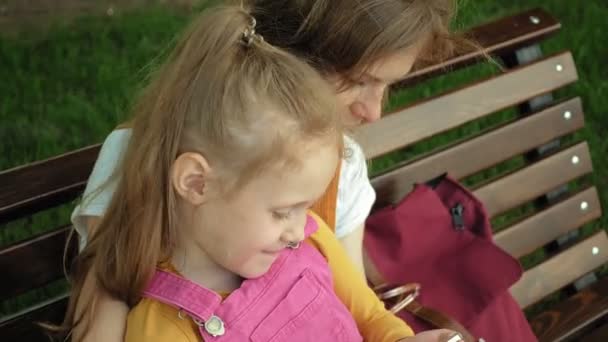 Η μαμά και η κόρη χρησιμοποιούν gadget στον ανοιχτό αέρα. Καλοκαίρι — Αρχείο Βίντεο