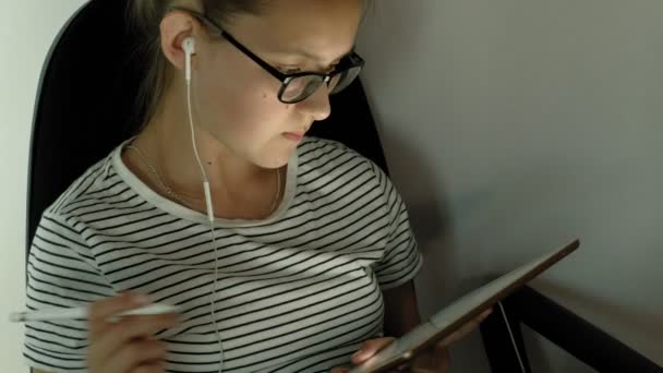 Chica adolescente utiliza la tableta con auriculares. Hora de la tarde. — Vídeos de Stock