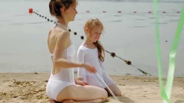 Mère et fille en maillots de bain blancs dansant avec un ruban de gymnastique sur une plage de sable fin. Été, aube — Video