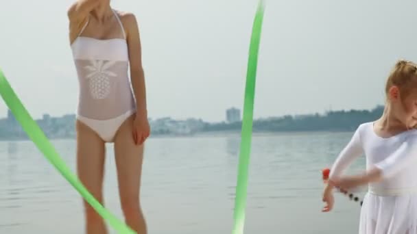 白い水着を着た母と娘が砂浜で体操のリボンで踊る。夏、夜明け — ストック動画