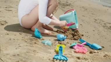 Kız çocuk kalıpheykeller kullanarak sahilde kum ile oynar. Güneşli bir yaz günü. Tatil