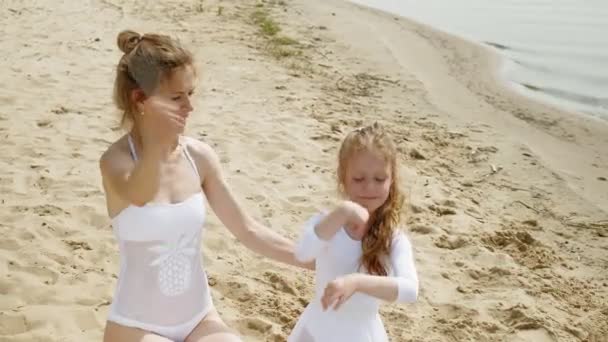 Μητέρα και κόρη σε λευκές μαγιό κοστούμια χορεύοντας με γυμναστική κορδέλα σε μια αμμώδη παραλία. Καλοκαίρι, αυγή — Αρχείο Βίντεο