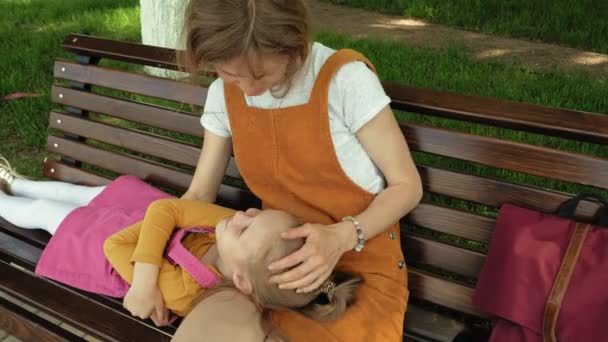 Mama z córką, Dziewczyna w wieku przedszkolnym leżącego na kolanach młodej kobiety w parku na ławce. Letni słoneczny dzień — Wideo stockowe