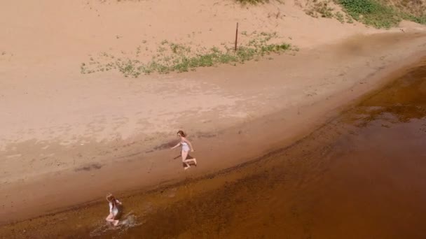 Мать и дочь бегут вдоль реки по песку. Пляж Солнечный летний день. Аэросъемка — стоковое видео