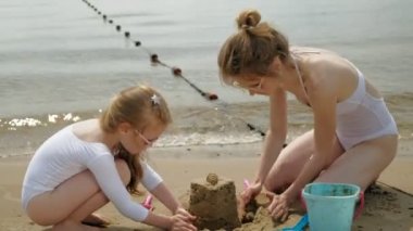Anne ve kızı sahilde kumdan bir kale inşa oynuyorlar. Yaz güneşli bir gün. Tatil