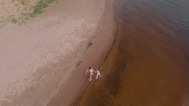 anne ve kızı kum boyunca nehir boyunca koşmak. Beach. Güneşli bir yaz günü. Hava çekimi