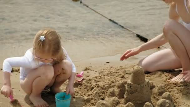 Mamá e hija están jugando en la playa, construyendo un castillo de arena. Día soleado de verano. vacaciones — Vídeos de Stock