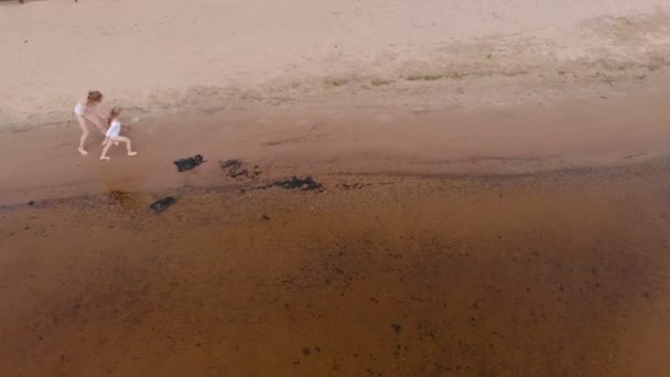 Μητέρα και κόρη τρέχουν κατά μήκος του ποταμού κατά μήκος της άμμου. Παραλία. Ηλιόλουστη καλοκαιρινή μέρα. Εναέρια γυρίσματα — Αρχείο Βίντεο
