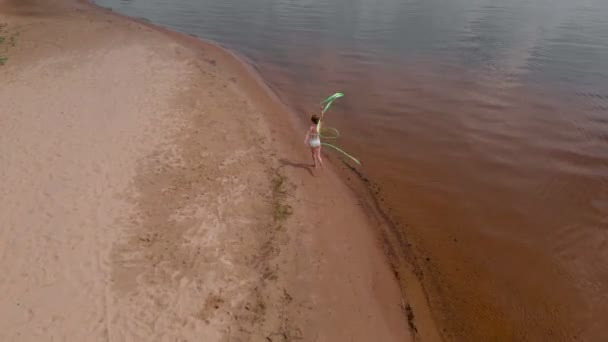 Mladá žena gymnastka v bílém těle na písečné pláži tančící s gymnastickou stuhou. Léto, svítání — Stock video