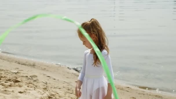 Gadis prasekolah dengan tarian sebuah pita senam di pantai berpasir. Musim panas, fajar — Stok Video