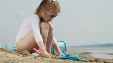 Kız çocuk kalıpheykeller kullanarak sahilde kum ile oynar. Güneşli bir yaz günü. Tatil