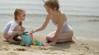 Anne ve kızı sahilde kumdan bir kale inşa oynuyorlar. Yaz güneşli bir gün. Tatil