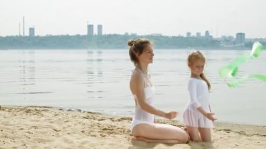 kumlu bir plajda jimnastik kurdele ile dans beyaz mayo lar içinde anne ve kızı. Yaz, şafak