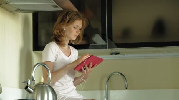 Mujer con auriculares en la cocina utiliza la tableta. Buenos días. — Vídeos de Stock