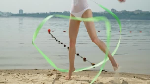 Jeune femme gymnaste dans un corps blanc sur une plage de sable dansant avec ruban de gymnastique. Été, aube — Video