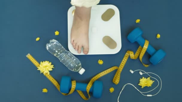Γυναικεία γεμάτα γυμνά πόδια στέκονται στη ζυγαριά σε μπλε φόντο. Δίαιτα, γυμναστική — Αρχείο Βίντεο