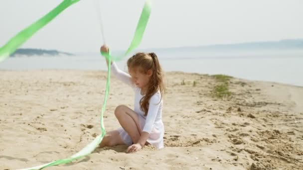 Niña preescolar con bailes de una cinta de gimnasia en una playa de arena. Verano, amanecer — Vídeo de stock