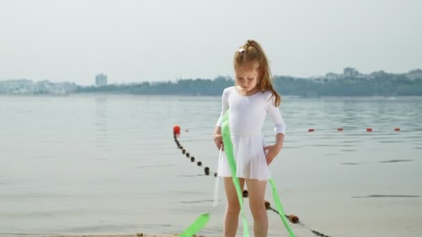 Menina pré-escolar com danças uma fita ginástica em uma praia arenosa. Verão, amanhecer — Vídeo de Stock