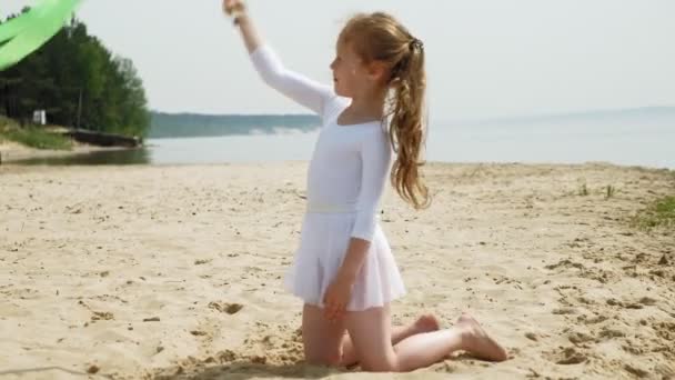 Preschool girl with dances a  gymnastic ribbon on a sandy beach. Summer, dawn — Stock Video