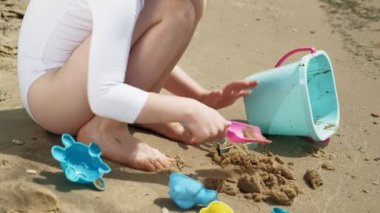 Kız çocuk kalıpheykeller kullanarak sahilde kum ile oynar. Güneşli bir yaz günü. Tatil