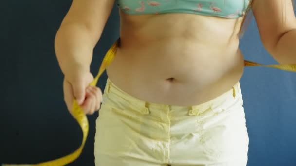 Dikke buik van een vrouw close-up op een blauwe achtergrond. Schadelijk voedsel, obesitas — Stockvideo