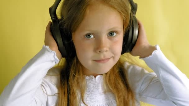 Cheerful little girl in headphones on a yellow background. Closeup portrait. — Stock Video